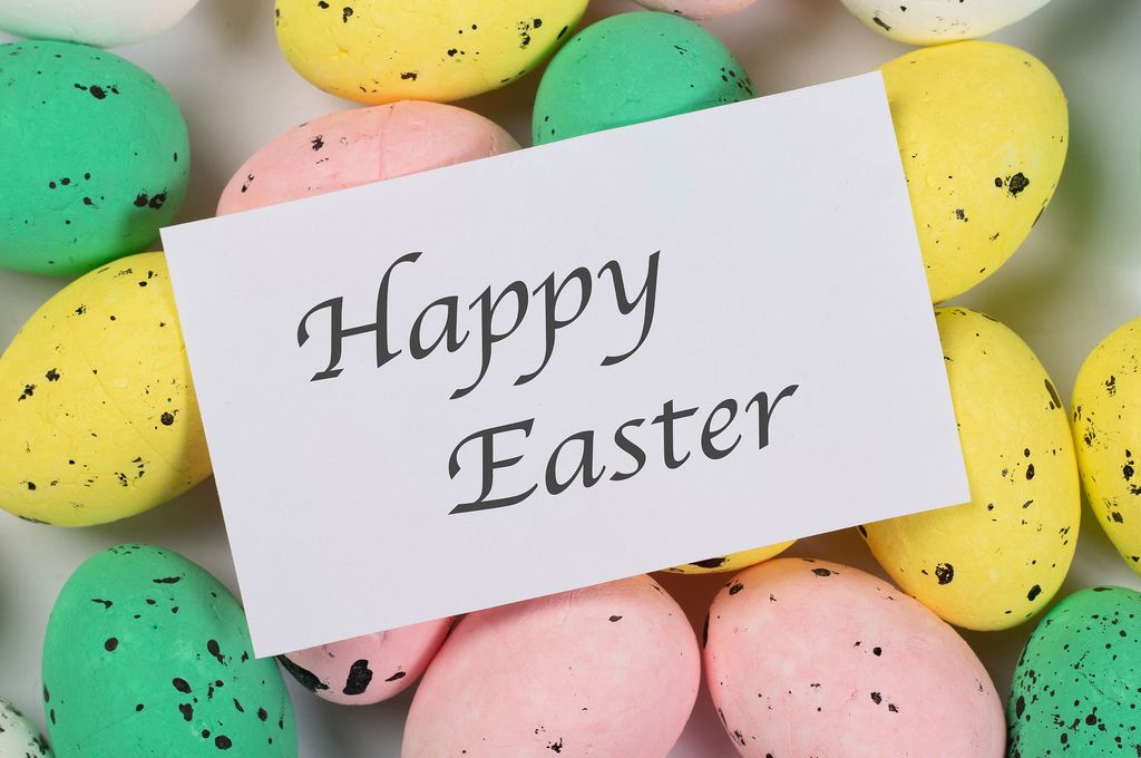 Ostergruß HAPPY EASTER (frohe Ostern) auf weißem Papier liegt auf farbigen Ostereiern