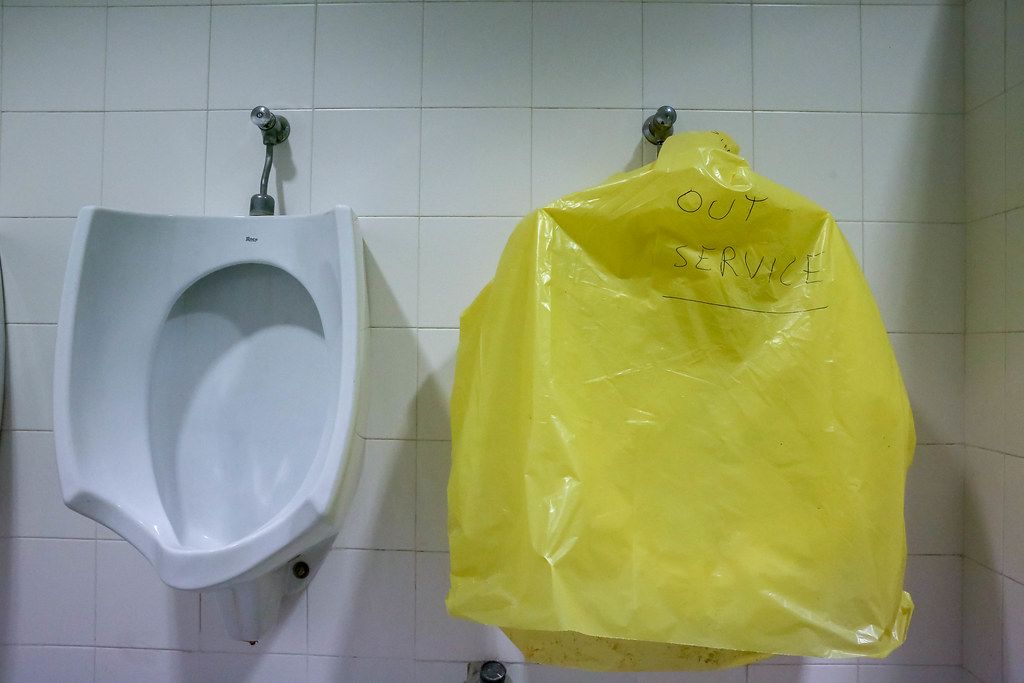 Out of Service - Schriftzug auf gelber Folie zeigt defektes Pissoir neben einem funktionierenden Urinal auf einer Herrentoilette in Barcelona, Spanien
