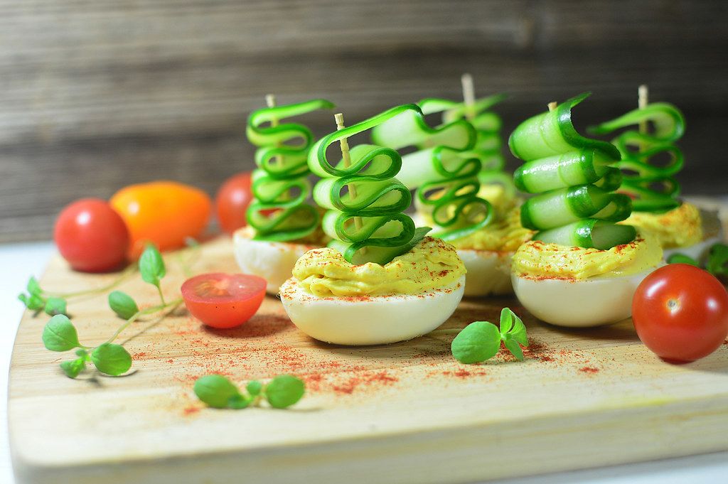 Party food: boiled eggs stuffed and topped by cucumber slices, served on a wooden board with cherry tomatoes and basil leaves