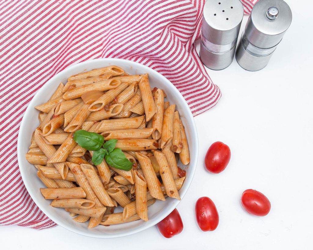 Pasta mit Tomatensoße und Basilikum neben ganzen Cherrytomaten und Salz- und Pfeffermühle