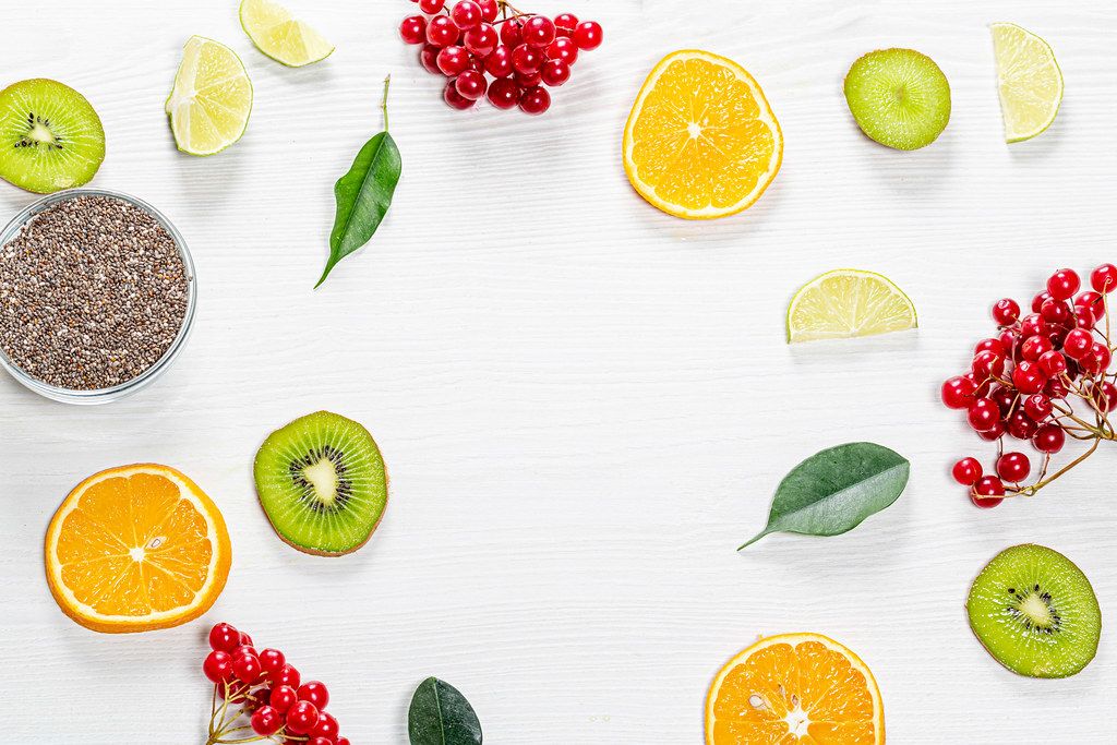 Pieces of fresh fruit, berries and green leaves with Chia seeds on a white wooden background. Top view