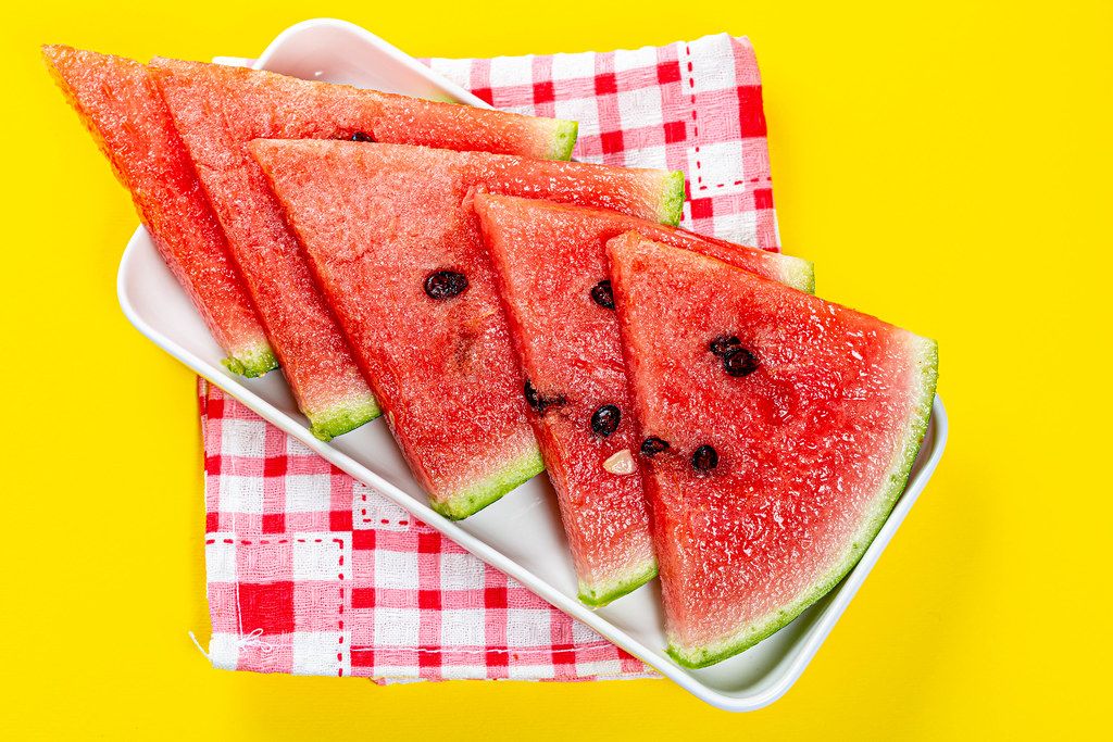 Pieces of ripe fresh watermelon on a yellow background with a kitchen towel
