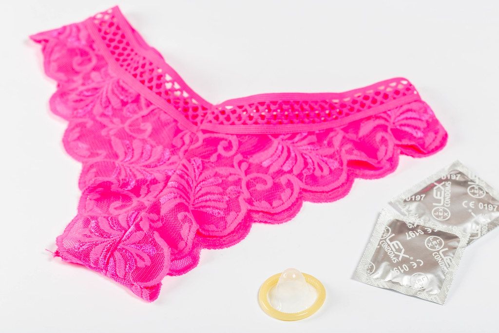 Pink women's panties and condoms on white background