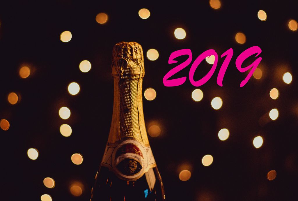 Pinker Schriftzug 2019 neben ungeöffneter Champagnerflasche und Lichteffekten auf dunklem Hintergrund