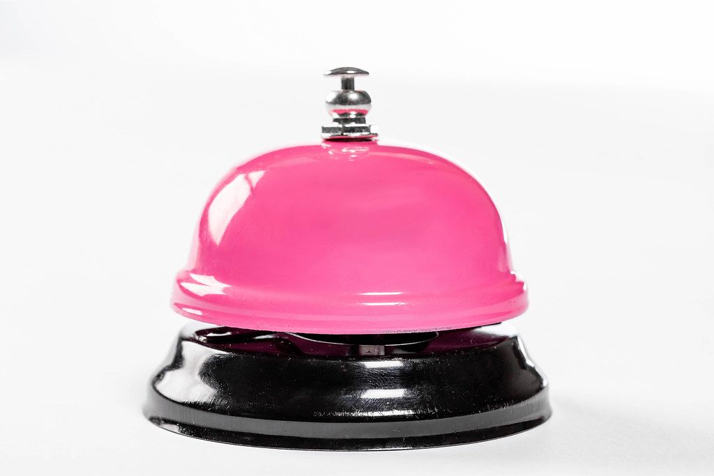 Pinkfarbene Hotel-Service-Glocke vor weißem Hintergrund