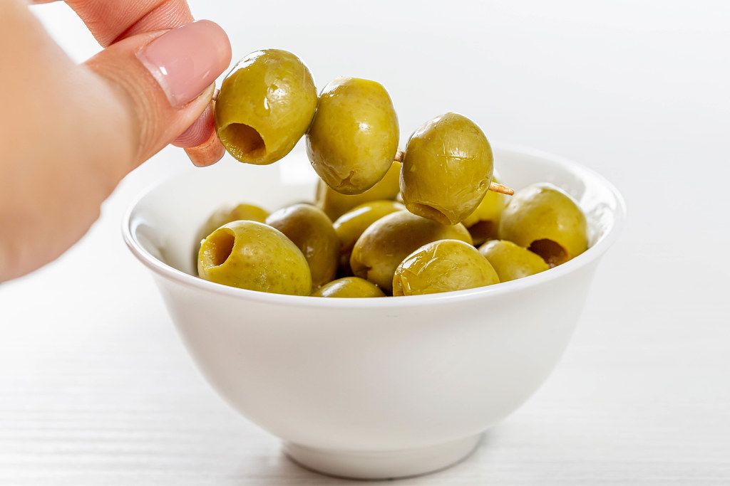 Pitted green olives in bowl on white background