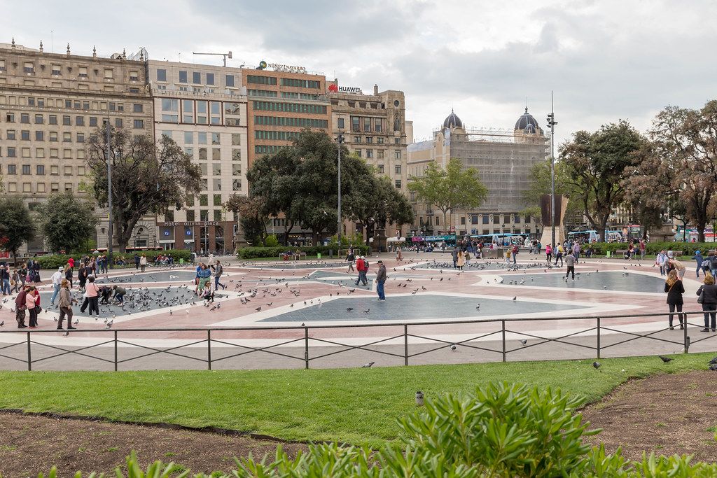 Placa de Catalunya with pigeons and people on star-shaped pattern of red-blue floor tiles in Barcelona, Spain