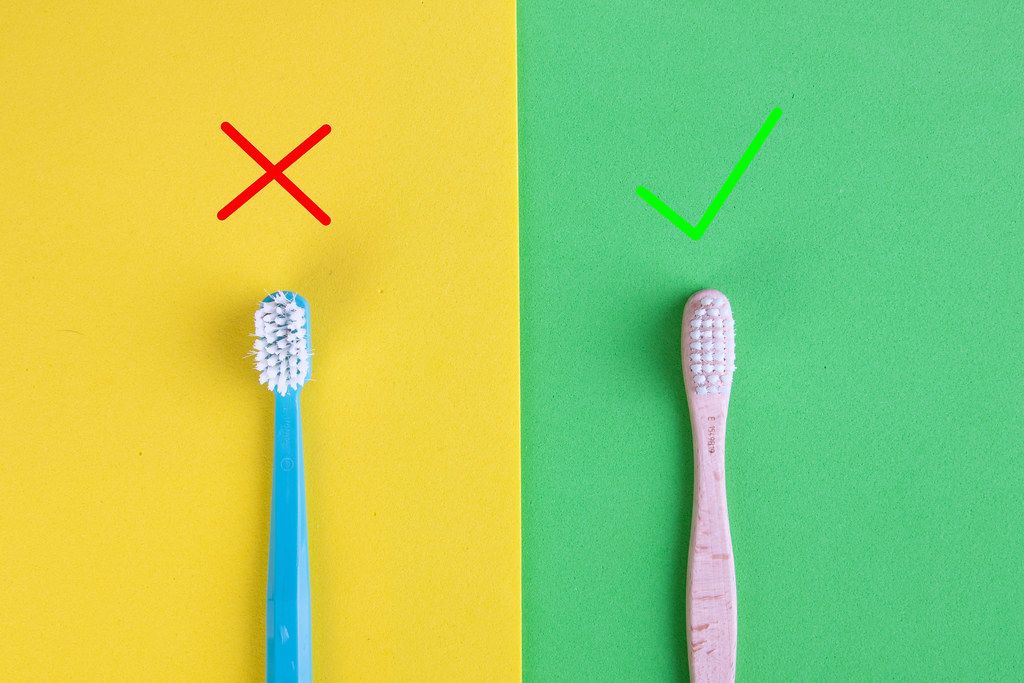 Plastic and bamboo toothbrushes on yellow and green background