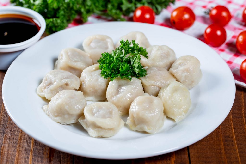 Plate of dumplings with sauce, herbs and cherry tomatoes