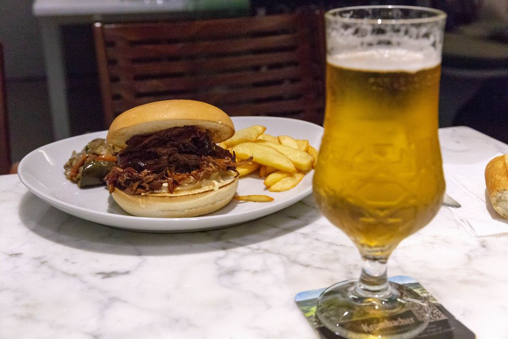Pulled Beef Burger mit Pommes und Gemüse auf einem weißen Teller mit einem Glas Bier