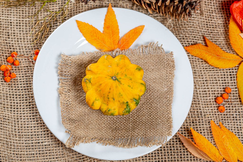 Pumpkin on a plate with autumn leaves, berries and cones. Autumn holidays background