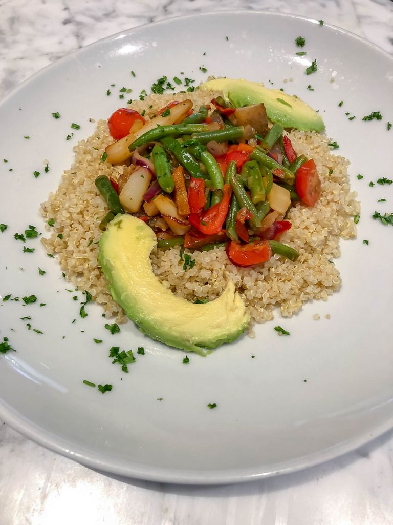 Quinoa mit blanchiertem Gemüse und Avocado auf einem weißen Teller mit Petersilie garniert