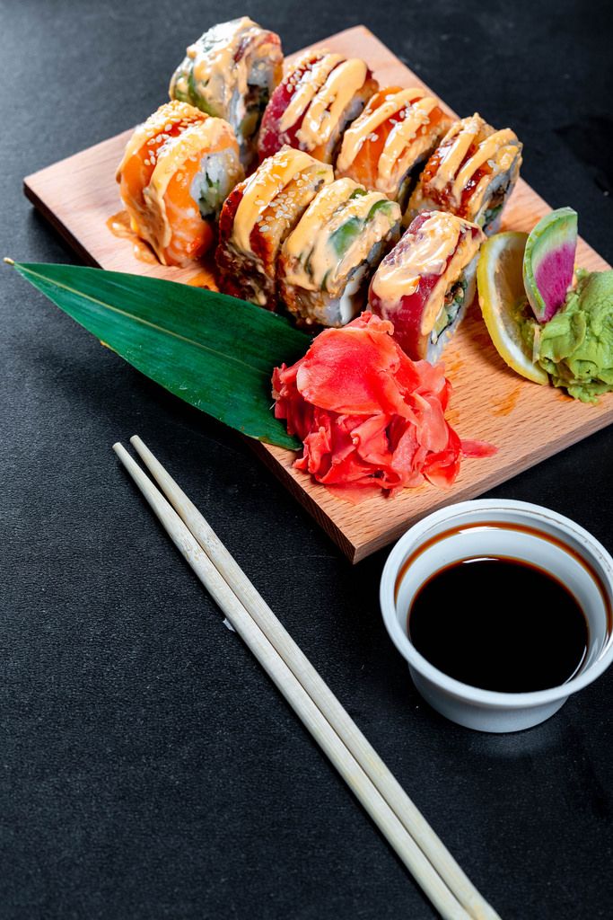 Rainbpw Dragon Sushi mit Sojasoße und Essstäbchen auf schwarzem Hintergrund