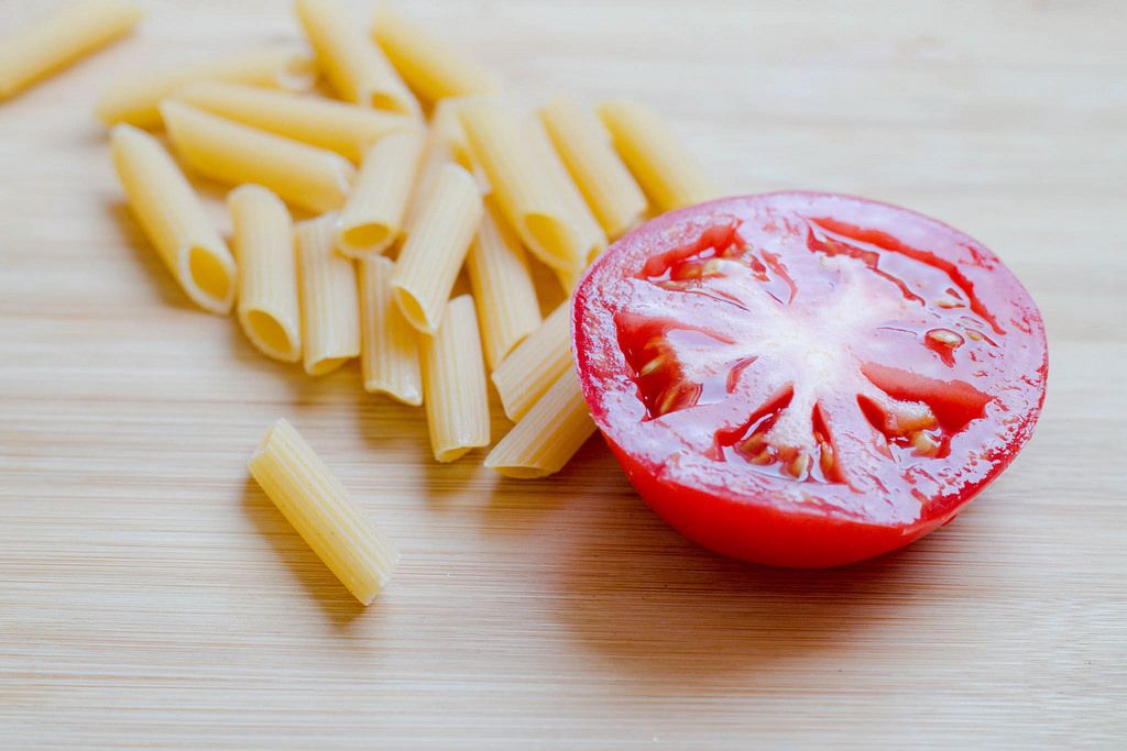 Raw pasta and a tomato on wooden background, kitchen