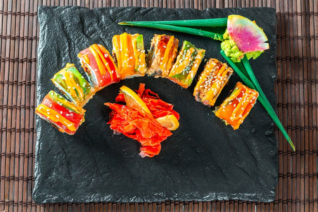 Regenbogen-Drachen-Sushirolle mit Wasabi und Ingwer geschnitten auf schwarzer Steinplatte