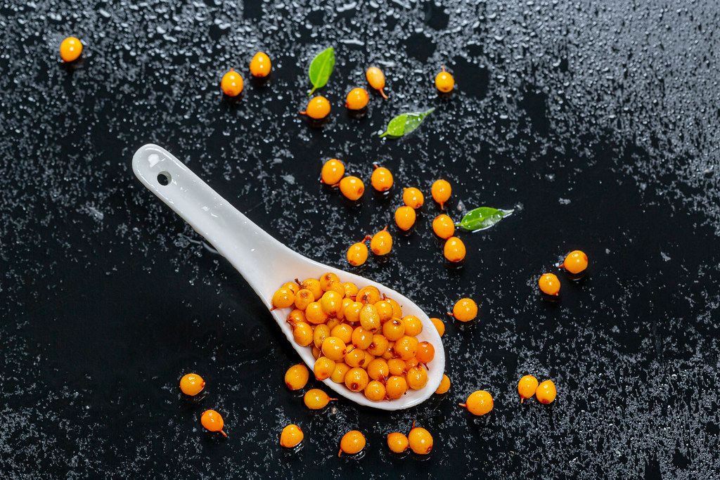 Ripe fruits of sea buckthorn with drops of water on a black background. View from above