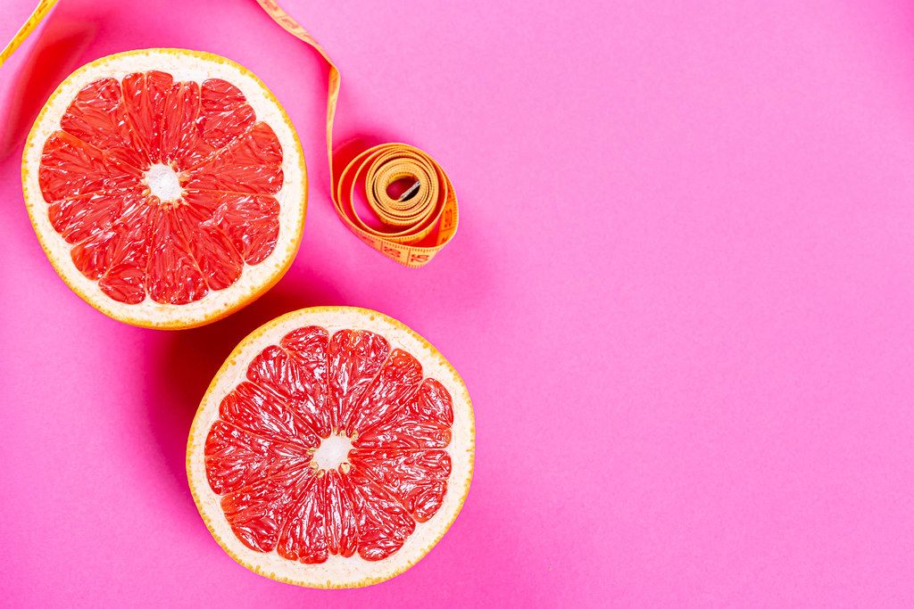 Ripe half of pink grapefruit citrus fruit on pink background with measuring tape