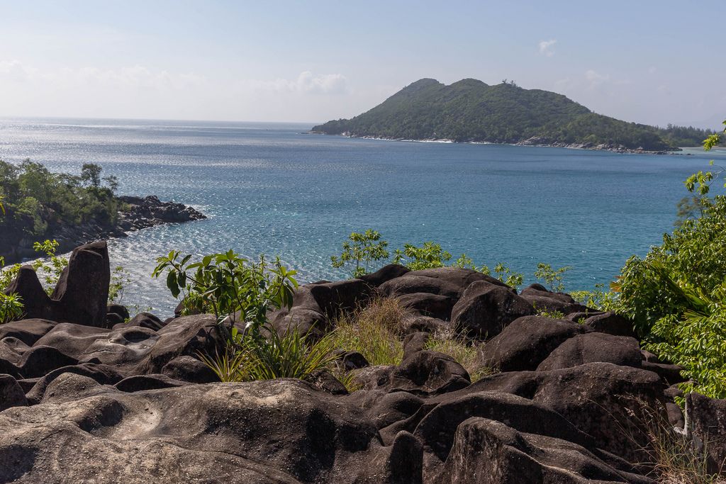 Ros Lepas schwarze Granitfelsen an der Klippe von Pointe Paul auf Mahé (Seychellen) mit Blick auf Cap Ternay im Indischen Ozean