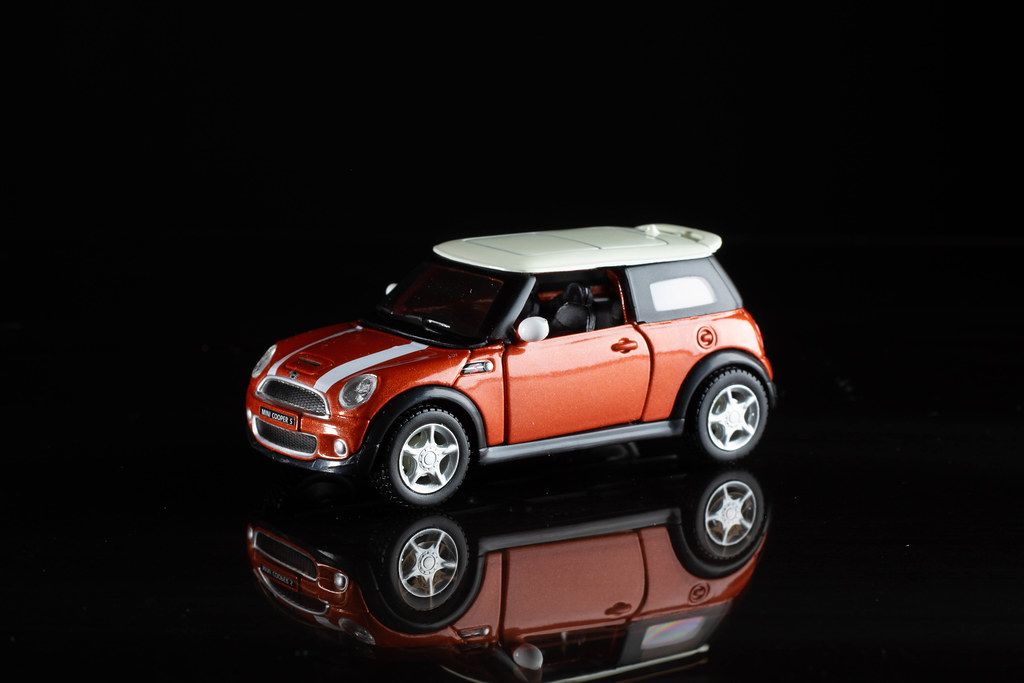 Roter Mini Cooper S mit weißem Dach und Streifen als Spielzeugauto vor schwarzem Hintergrund