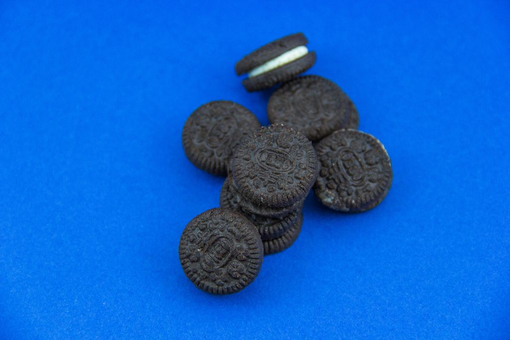 Runde Schokoladenkekse mit weißer Cremefüllung auf blauem Untergrund