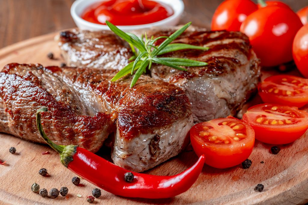 Saftig gebratene Steaks mit Cherrytomaten, Chili, Pfefferkörnern und Rosmarin auf Holzbrett