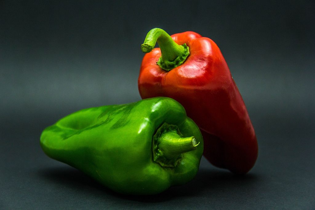 Saftige, rote und grüne ganze Paprika vor dunklem Hintergrund