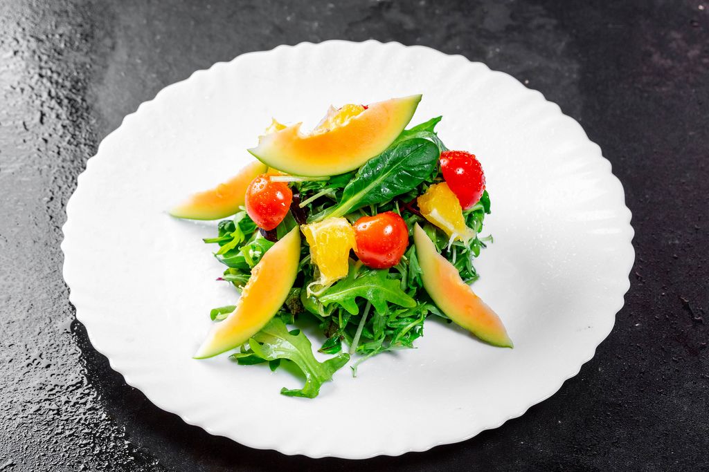 Salad with fresh avocado, cherry tomatoes, orange slices and arugula leaves