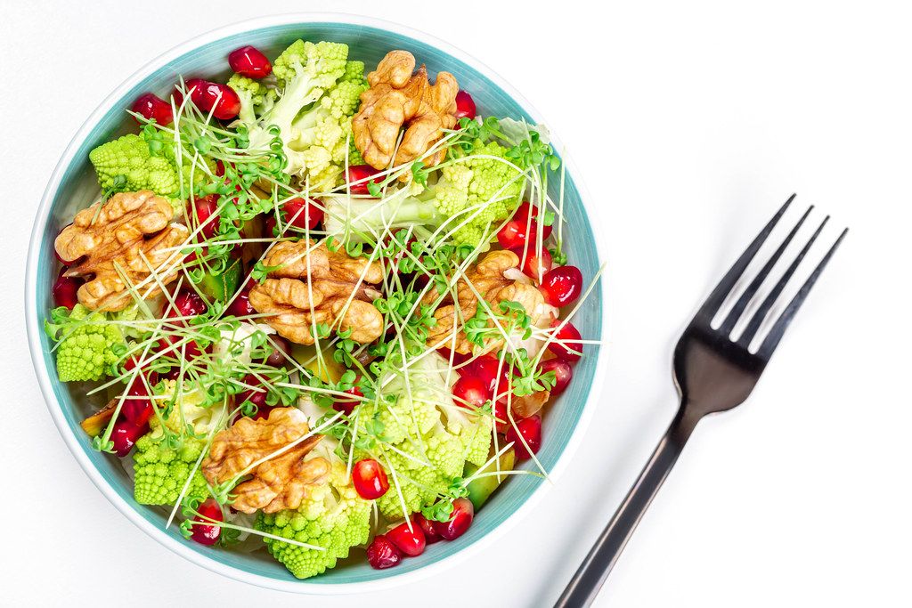 Salad with walnuts, pomegranate, watercress and vegetables on a white background, top view