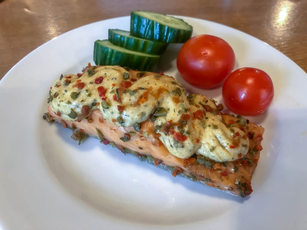 Salmon filet with topping, fresh herbs, tomatoes and cucumber on a white plate in Berlin-Köpenick, Pentahotel