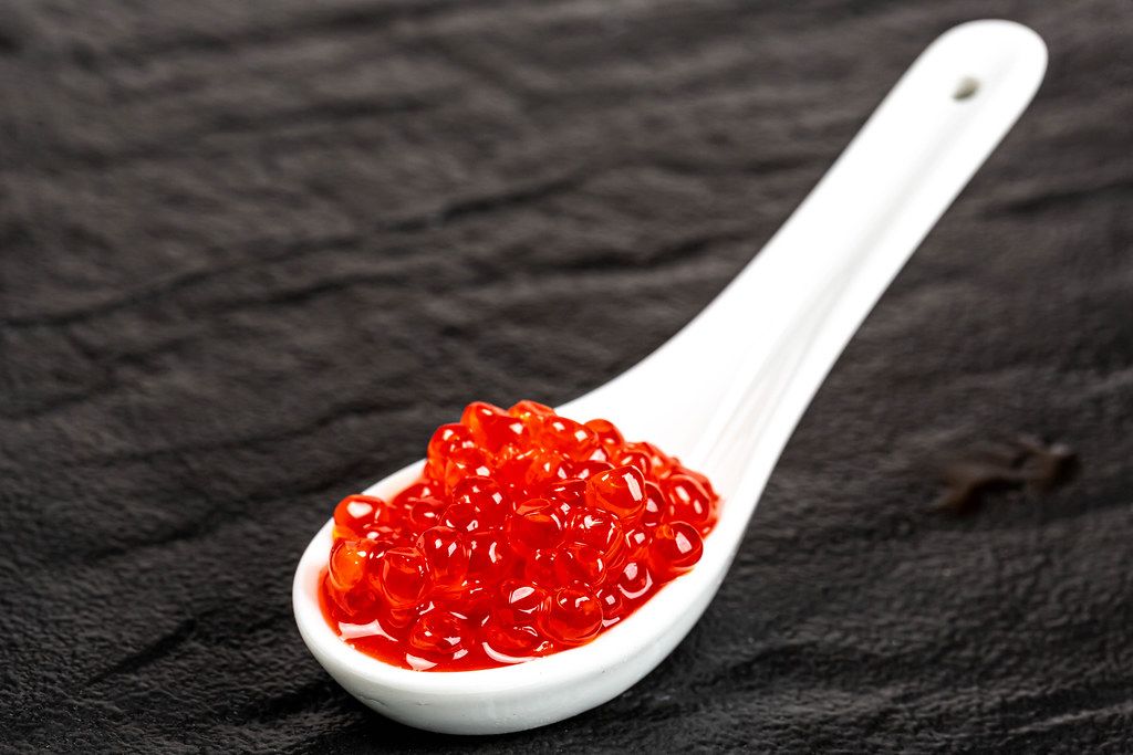 Salted red caviar in a white spoon on a black stone background