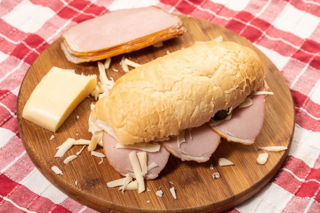 Sandwich mit knusprigem Brötchen auf Holzbrett mit Zutaten wie Schinken und Käsestück