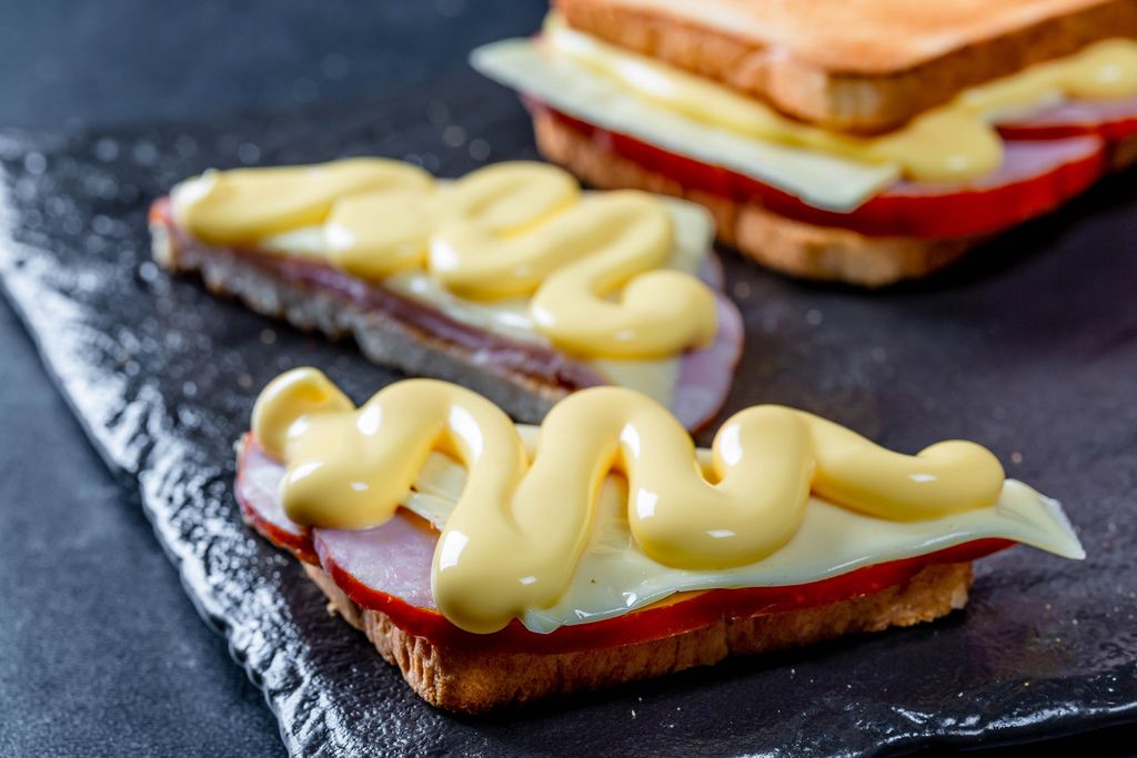 Sandwiches with meat, cheese and cheese sauce on a black stone
