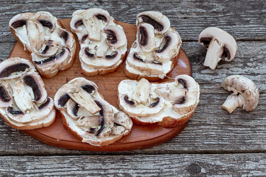 Sandwiches with mushrooms before baking on an old wooden background. The view from the top
