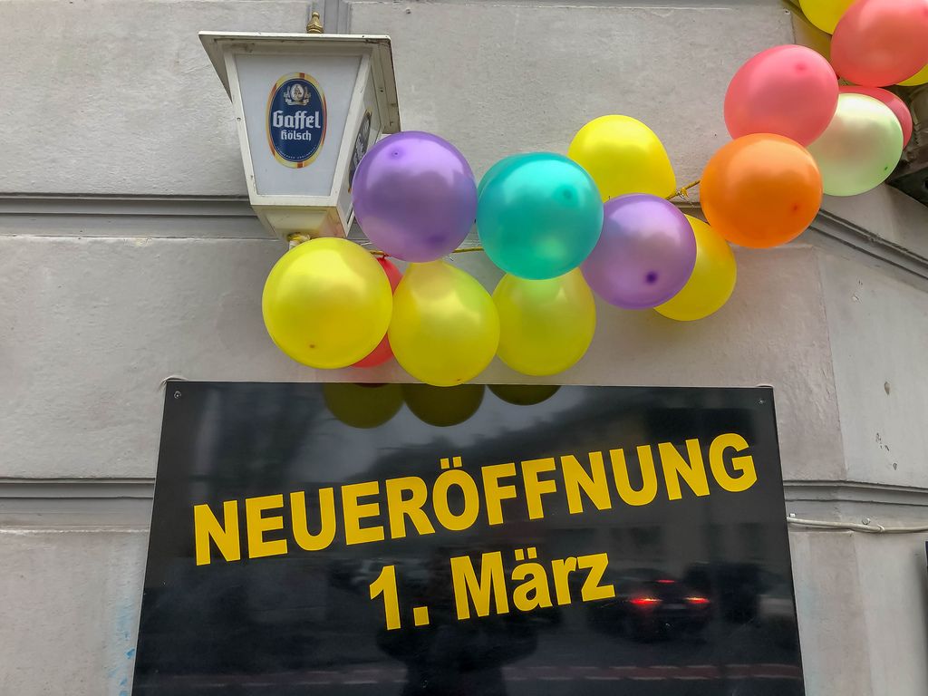 Schild an Hauswand zeigt Neueröffnung am 1. März mit Luftballons und Gaffel Kölsch Werbung auf Lampe