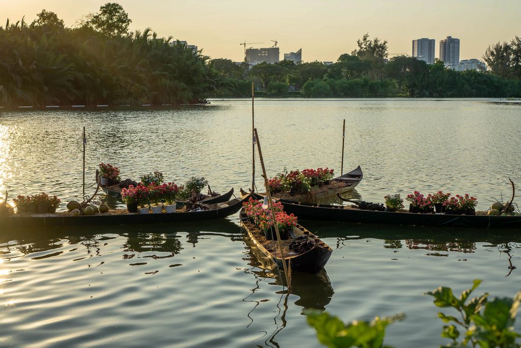 Schmale Holzboote mit Blumen auf See in Ho Chi Minh City mit Sonnenuntergang über Hochhäusern