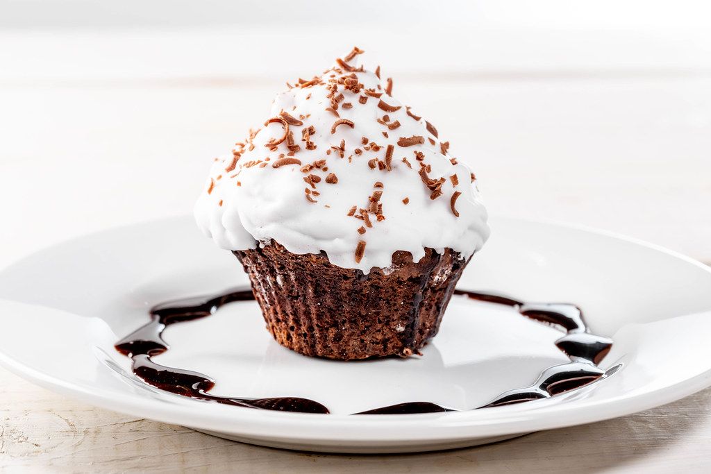 Schokoladen-Muffin mit weißer Sahnecreme und Schokostreuseln als süßer Nachtisch
