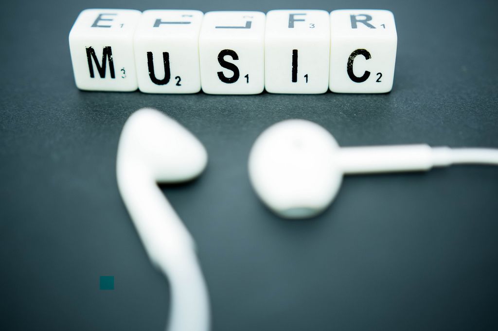 Schriftzug MUSIC dargestellt mit weißen Würfeln neben weißen In-Ear-Kopfhörern