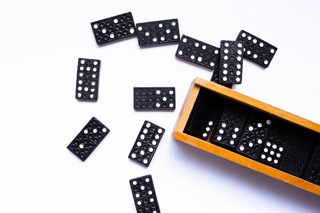 Schwarz-weiße Dominosteine liegen neben Holzkiste auf weißem Tisch