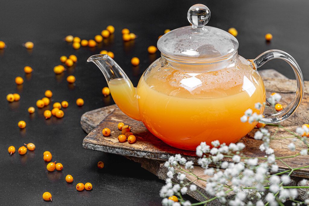Sea buckthorn hot drink in a teapot with fresh berries on a black background