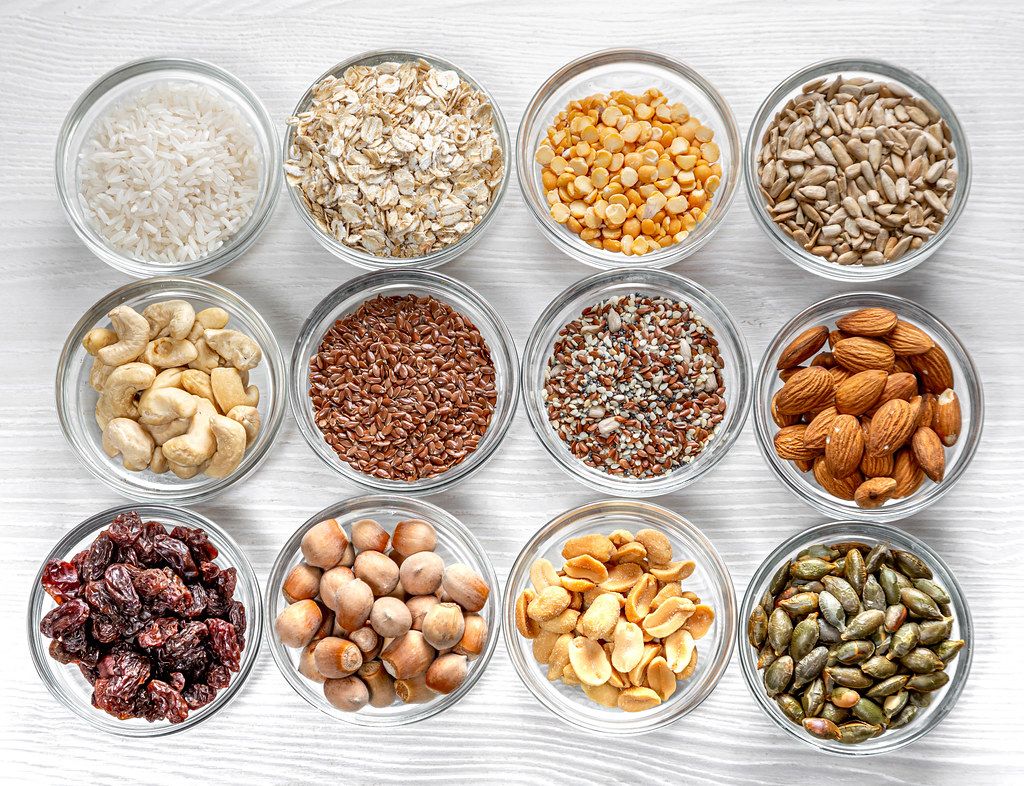 Seeds, nuts, grains in glass bowls on a white wooden background. Top view (Flip 2019)