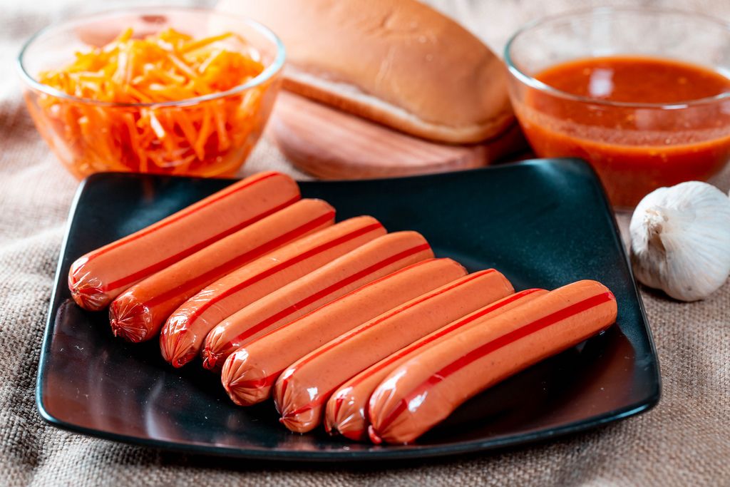 Set-up für Hotdogs mit ungekochten Würsten, Brötchen, marinierten Karotten, Ketchup und Knoblauch
