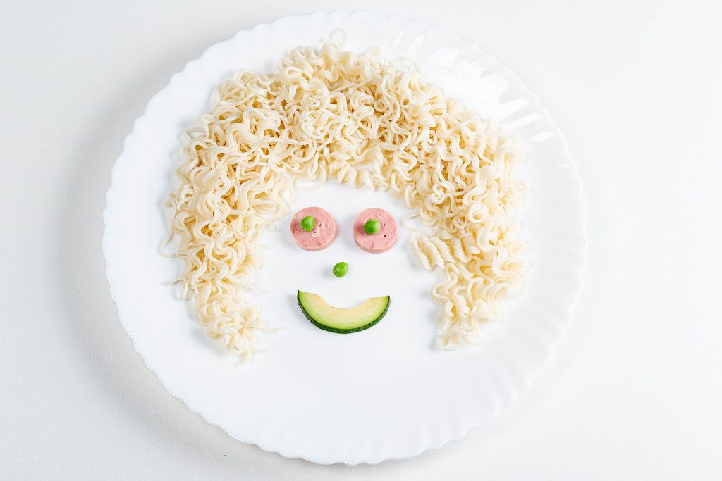 Smiling face made of macaroni, sausage, avocado slice and green peas