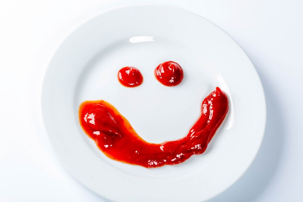 Smiling face painted with ketchup on a white plate