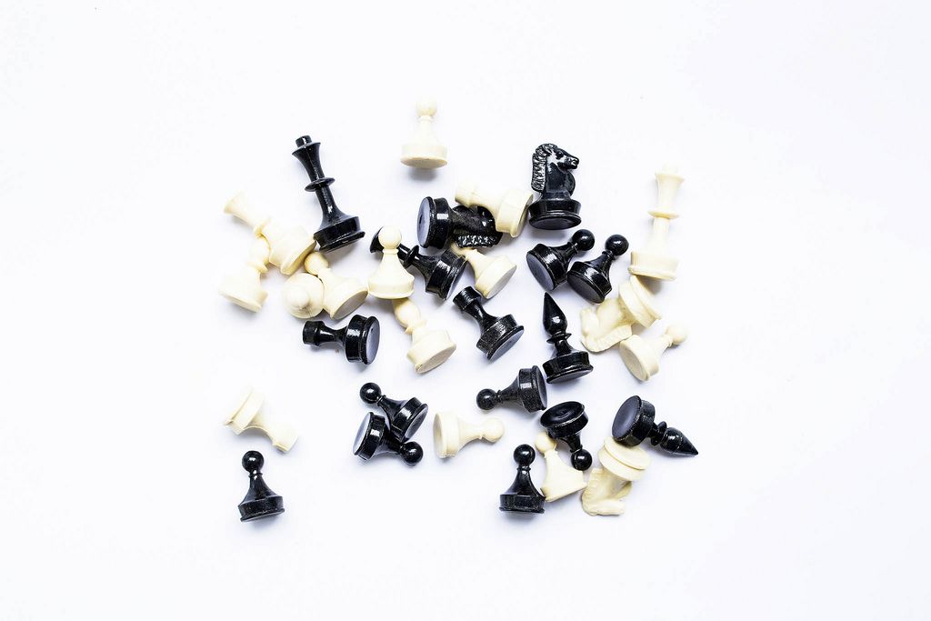 Sortiment aus schwarzen und weißen Schachfiguren verteilt auf weißem Hintergrund