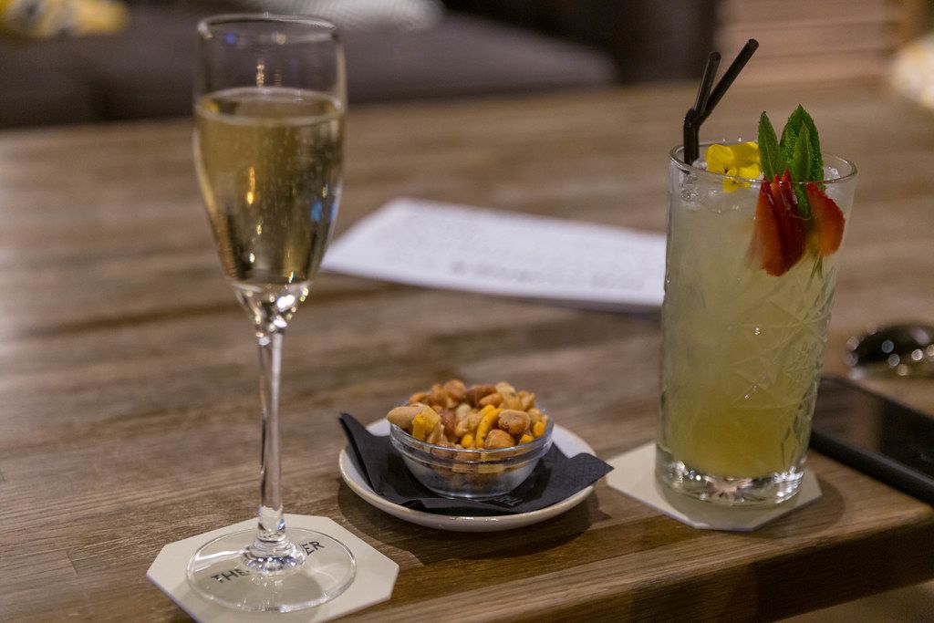 Sparkling wine, cocktail, mobile phone and small bowl of nuts on a rustic wooden table in the lounge and bar of The Corner Hotel in Barcelona, Spain