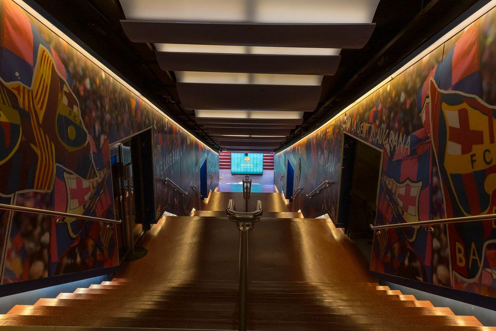 Spielertunnel des FC Barcelona mit aufgemalten Vereinsflaggen an den Wänden und beleuchtetem Treppengang zum Stadion Camp Nou in Spanien
