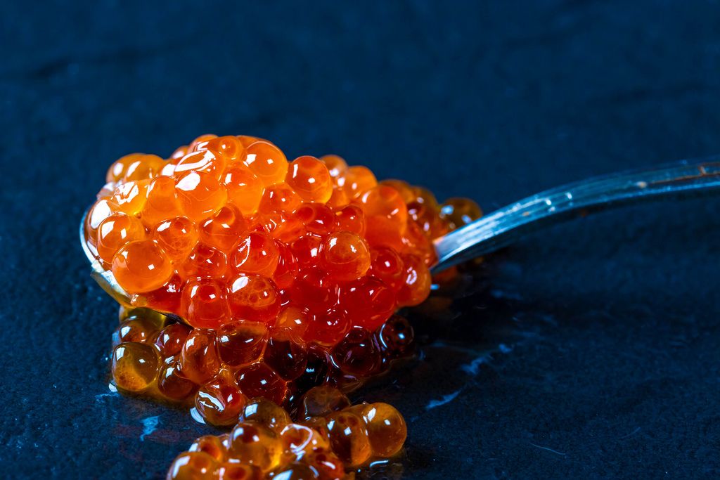 Spoon of red caviar on black background