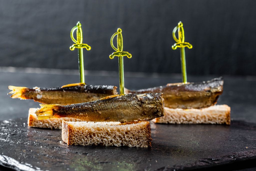 Sprat canape with brown bread on black background