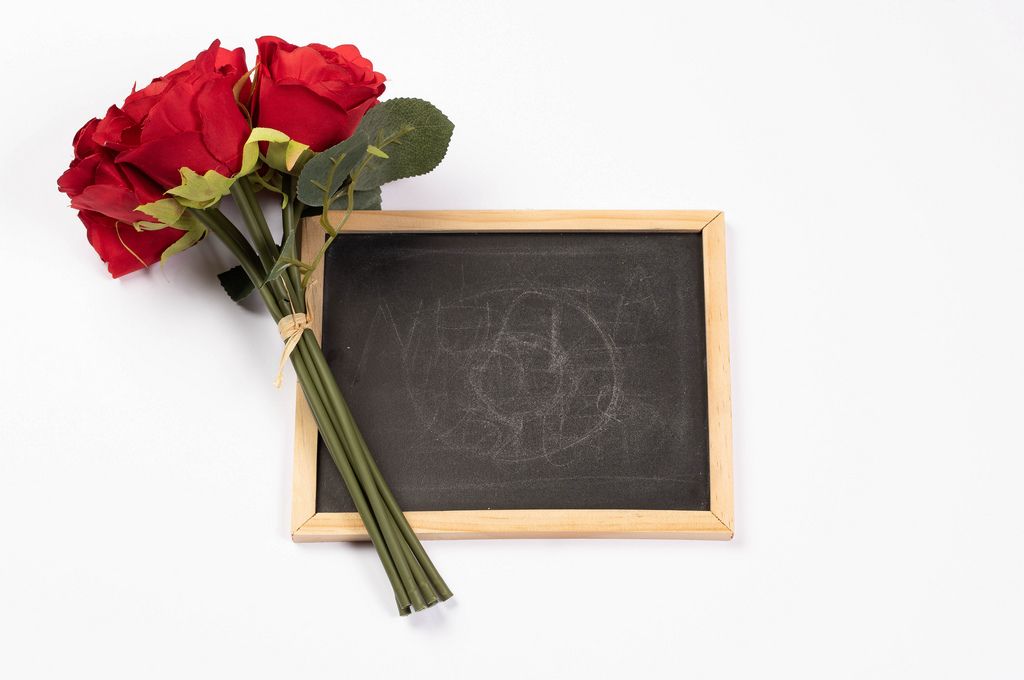 Strauß rote Rosen neben leerer schwarzer Kreidetafel vor weißem Hintergrund