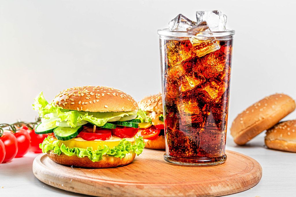 Street food concept - a glass of Coca Cola and hamburgers on a white wooden table